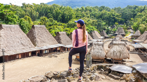 A young woman with a purple scarf admiring the Beno village in Flores, Indonesia. There are many small houses behind him. Each house is made of natural parts like wood and straw. History and tradition photo