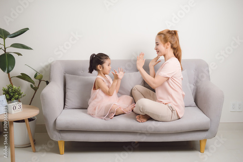 Happy young woman playing clapping game with female child while sitting in livingroom