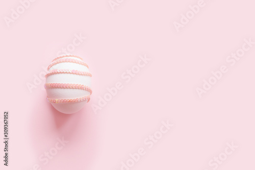 Easter egg decorated with mother of pearl sequin strip on a pastel pink background