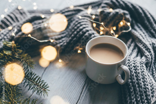Winter cozy composition coffee cup warm knitted scarf and christmas tree twigs. Selective focus.