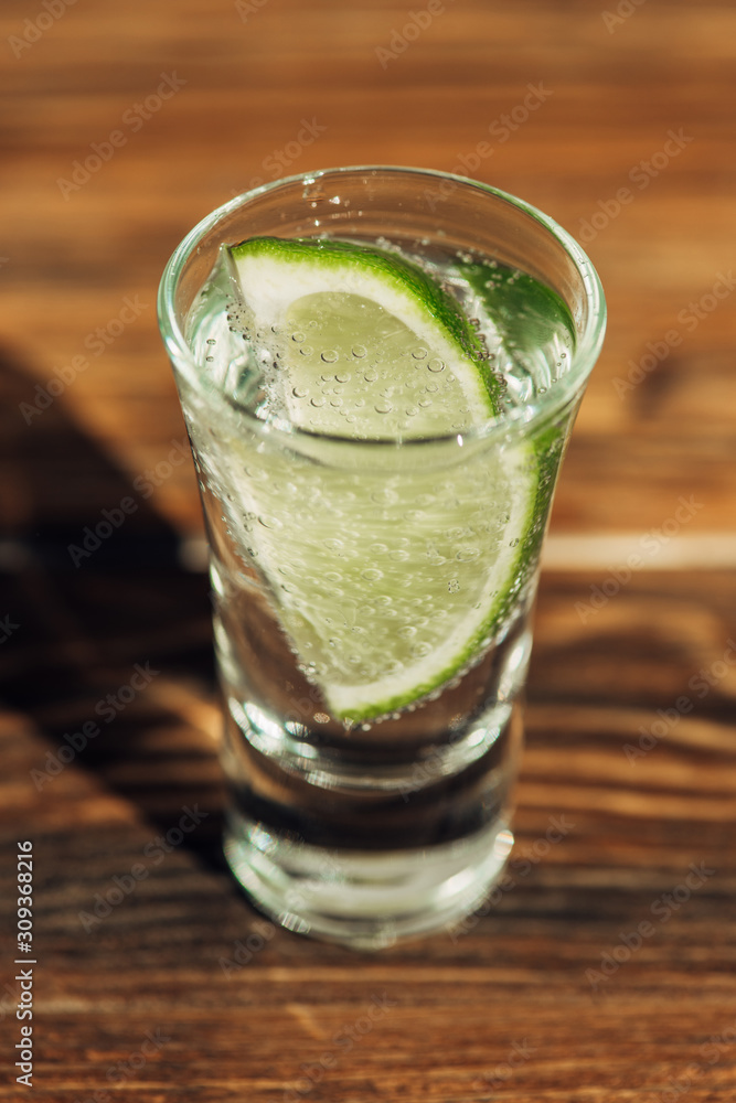 close up view of fresh tequila with lime on wooden surface in sunlight close up view of fresh tequila with lime on wooden surface in sunlight