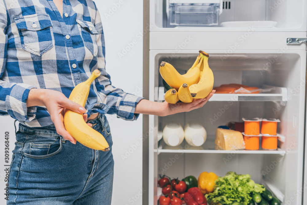 cropped view of woman holding bananas near open fridge with fresh food on shelves isolated on white cropped view of woman holding bananas near open fridge with fresh food on shelves isolated on white