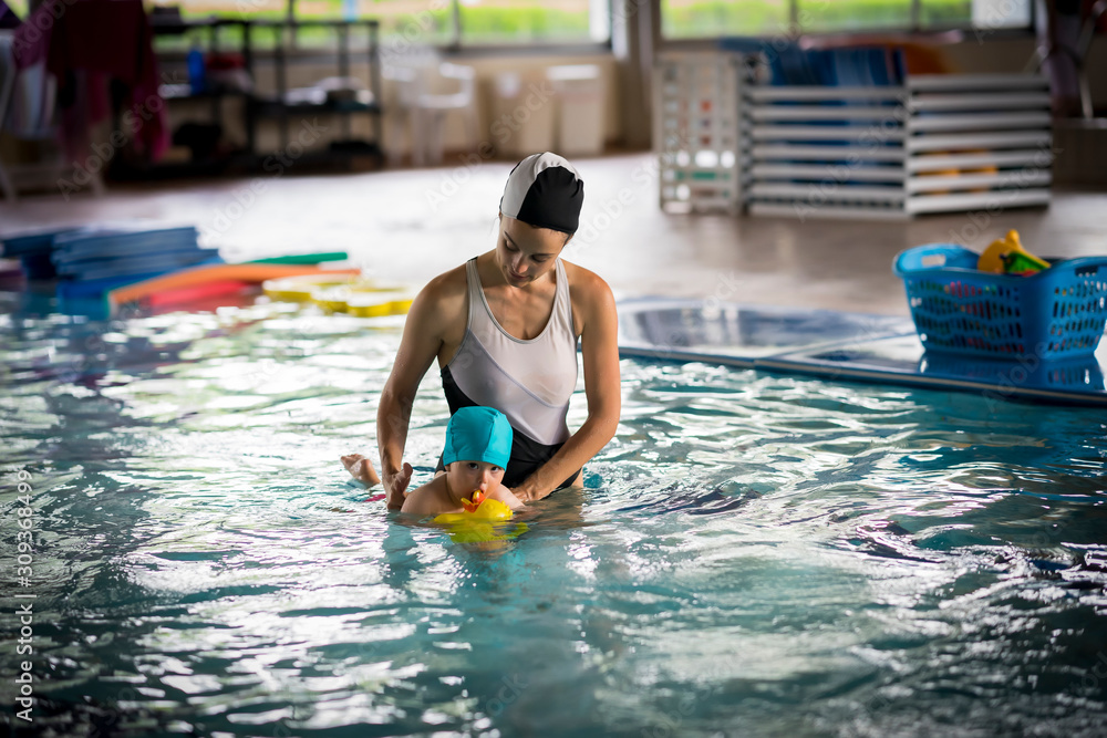 Girl in the middle of the indoor pool teaching a baby how to swim
