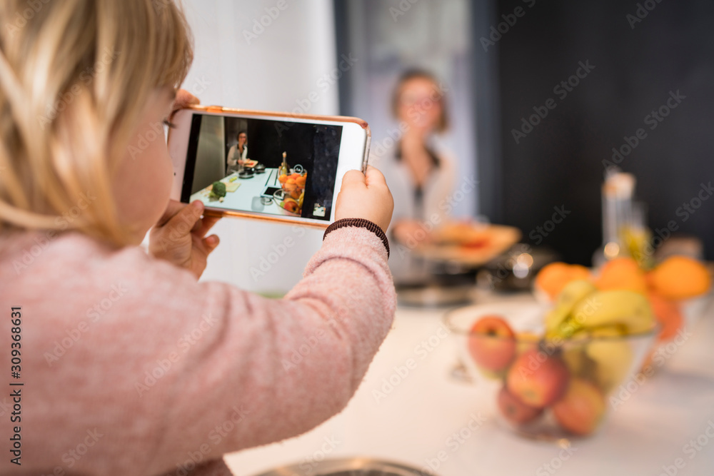Little girl taking a picture with her mother's mobile while cooking