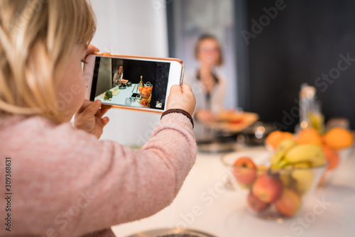 Obraz na płótnie Little girl taking a picture with her mother's mobile while cooking w salonie