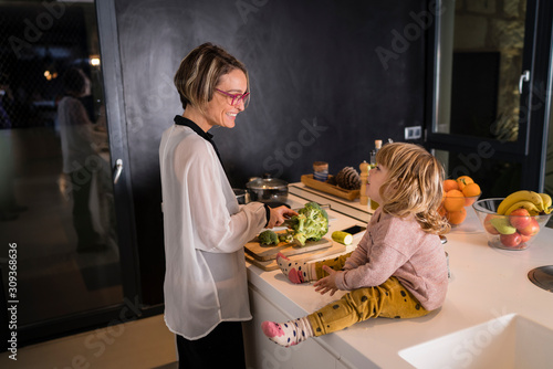 Obraz na płótnie Mother cutting vegetables in the kitchen talking to a little girl sitting next to her w salonie