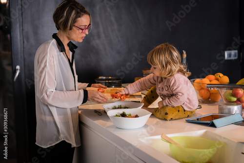 Obraz na płótnie Mother preparing two salad plates in the kitchen talking to a little girl sitting next to her who helps her w salonie
