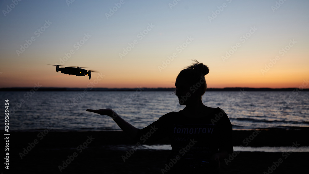 Silhouette of a girl with a drone on a beach during sunset