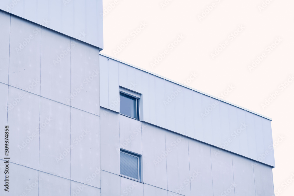 White and gray modern facade and top of an apartment building with two windows against the white sky. Seen in Germany in December White and gray modern facade and top of an apartment building with two windows against the white sky. Seen in Germany in December