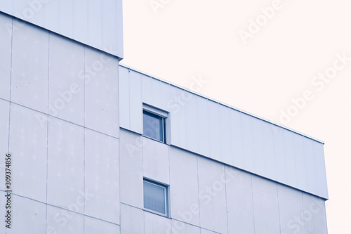 White and gray modern facade and top of an apartment building with two windows against the white sky. Seen in Germany in December
