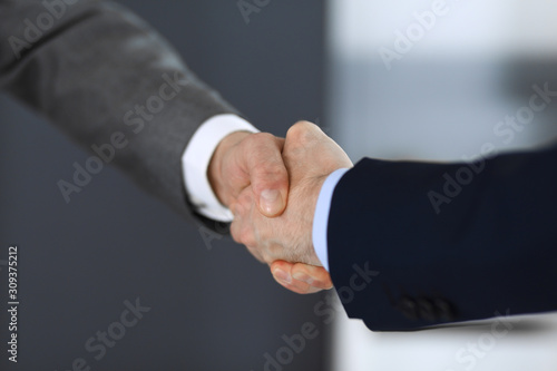 Business people shaking hands while standing with colleagues after meeting or negotiation, close-up. Group of unknown businessmen and women in modern office. Teamwork, partnership and handshake