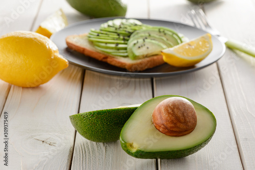 Avocado halves and toast with its slices on wooden table