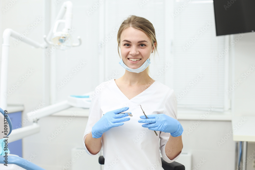 Smiling dentist stands in middle of cabinet with instruments in hands. Selective focus Smiling dentist stands in middle of cabinet with instruments in hands. Selective focus