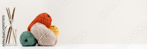 Multicolored bamboo wooden knitting needles in glass bottle and red, green, yellow and beige pastel colored balls of yarn. Copy space. Needlework and leisure concept. Template for your design.