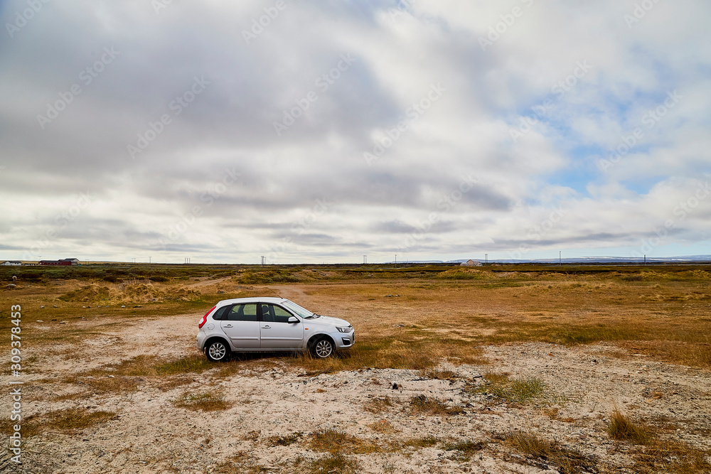 Tundra landscape with moss, glass and stouns in the north of Norway or Russia, car in it and blue sky with clouds