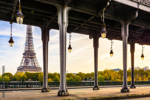 The Eiffel tower in Paris seen from the Bir-Hakeim bridge by a sunny morning with the glass globes of the Art Deco street lights and the metal pillars supporting the subway track in the foreground. photo