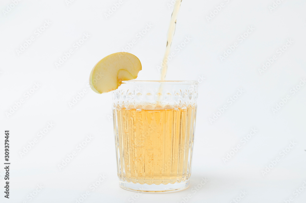 Pouring of sweet apple juice into the glass, slice of apple on the white background Pouring of sweet apple juice into the glass, slice of apple on the white background