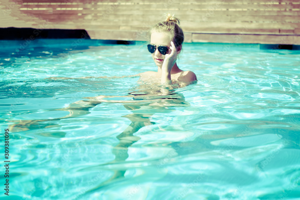 A young blonde posing in the water with glasses in selective focus