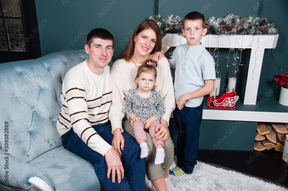 Family, parents and two beautiful children, boy and a girl, near the fireplace and Christmas tree on the sofa