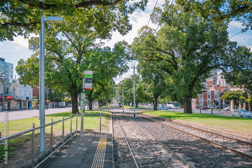 Tram stop on the straight rail road. A tram is entering from far away.