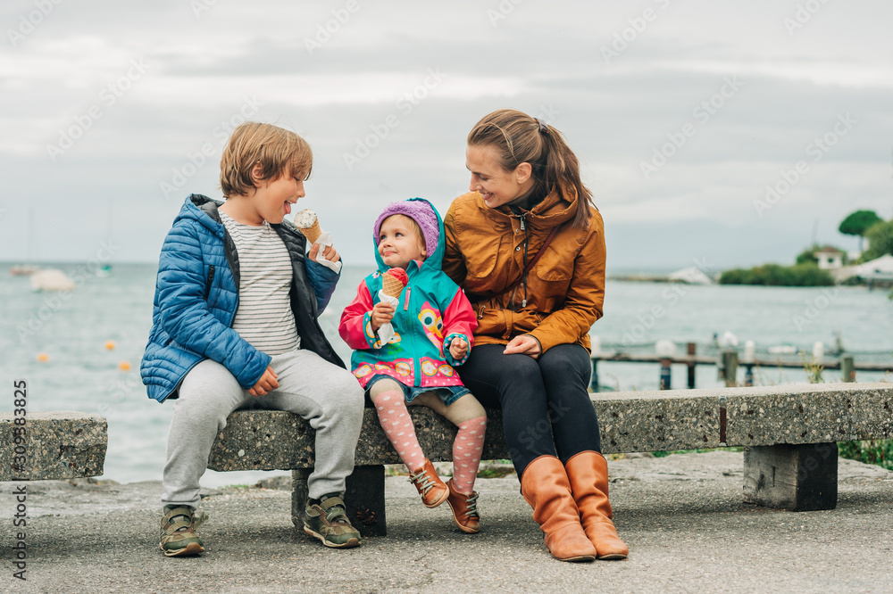 Φωτογραφία Two funny kids with mother eating ice cream by the lake on a rainy day