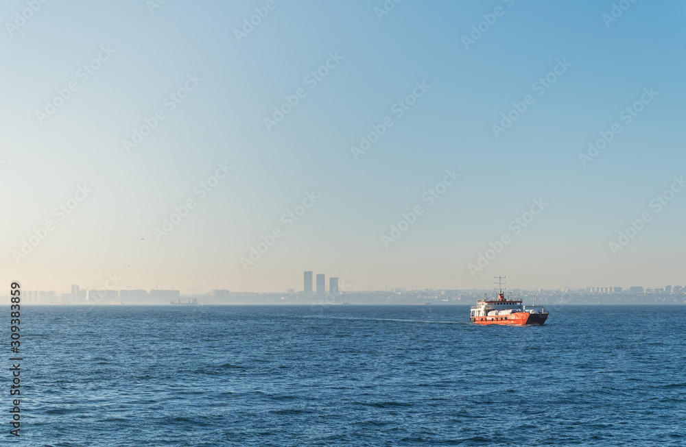 Fototapeta premium A lonely car ferry with trucks and tanks, in the waters of the Bosphorus, on a roadstead, against the backdrop of the cityscape of Istanbul.