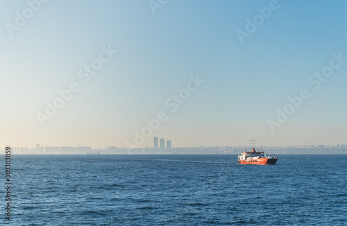 A lonely car ferry with trucks and tanks, in the waters of the Bosphorus, on a roadstead, against the backdrop of the cityscape of Istanbul.