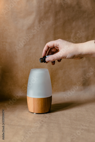 The hand of a woman puts a few drops of essential oils in a wooden diffuser