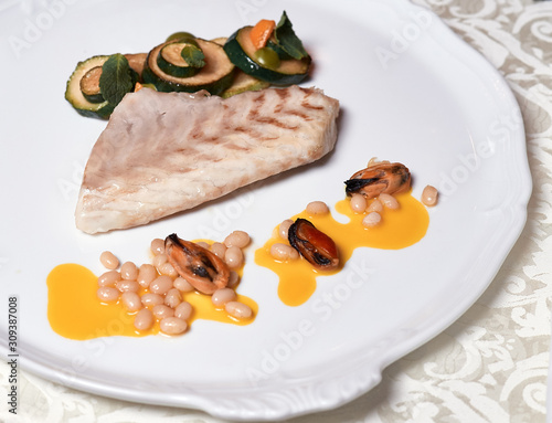 Roasted fish steak with mussels. Close up grilling Fish fillet with vegetables  and orange sauce decorated with cedre nuts on the white plate on the table. photo