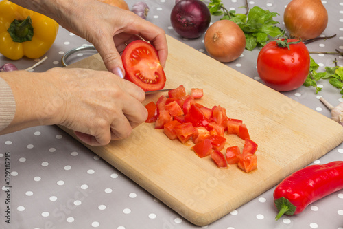 Hands chopped tomato. Red and yellow peppers, onions, garlic, herbs on the table. photo