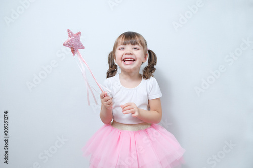 smiling little girl child holding a magic wand in his hand. A game of fairy, a sorceress. Performance of the play. Costume party