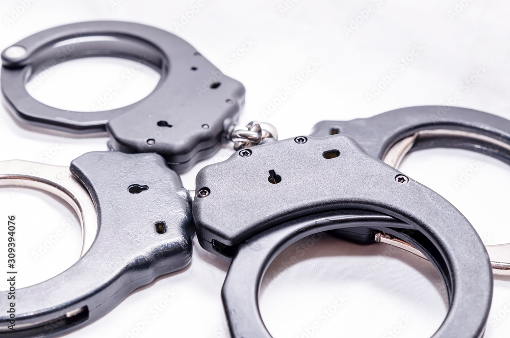 Two pair of handcuffs, one black and the other black and silver on a white background Two pair of handcuffs, one black and the other black and silver on a white background