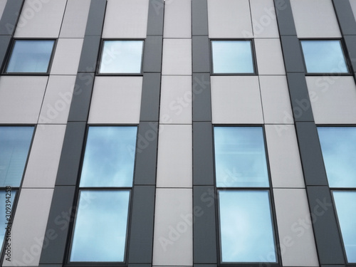 Windows with sky reflection. Generic elements of modern office architecture with linear pattern of parallel lines. Fragment of industrial building exterior featuring metal and plastic wall panels.