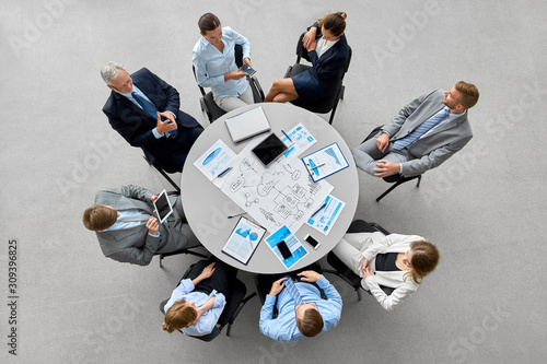 people, work and corporate concept - business team with gdgets and papers at round office table