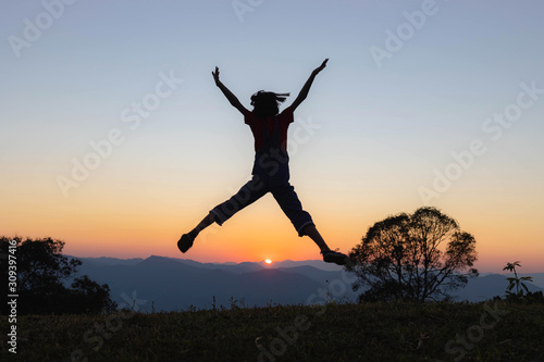 Silhouette of happy child jumping playing on mountain at sunset or sunrise