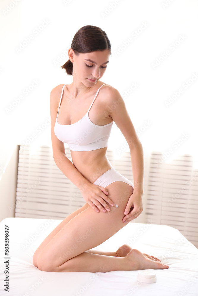 Foto de Close up shot of fit woman wearing only lingerie on white linen  bed, applying moisturizing lotion. Slim attractive female with flat belly  in white underwear in bedroom. Copy space for