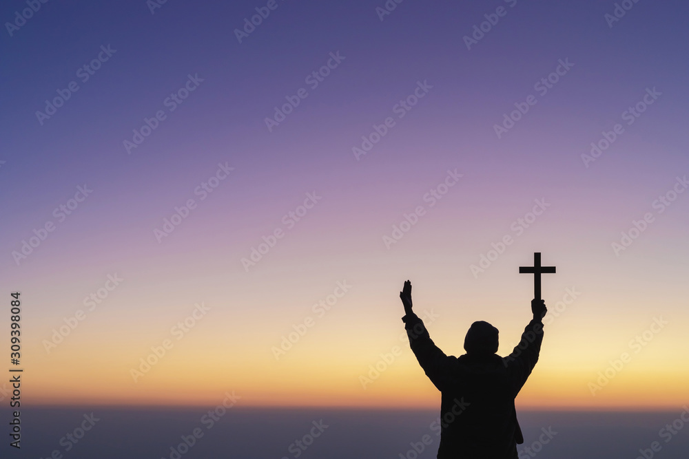 Human praying and holding christian cross for worshipping God at sunset sky background.Christian, Christianity, Religion copy space background.