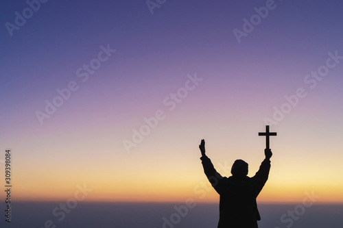 Human praying and holding christian cross for worshipping God at sunset sky background.Christian, Christianity, Religion copy space background.