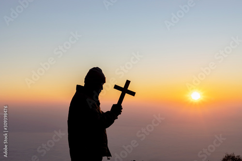 Silhouette human praying and holding christian cross for worshipping God at sunset or sunrise background.Christian, Christianity, Religion copy space background.