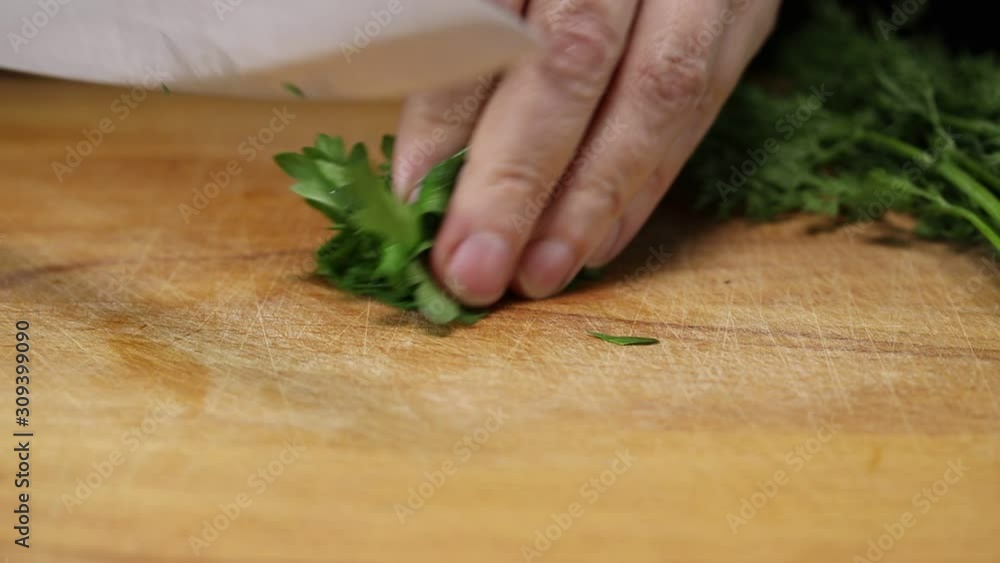 Woman thinly slices a bunch of parsley with a large kitchen knife on a cutting board Woman thinly slices a bunch of parsley with a large kitchen knife on a cutting board