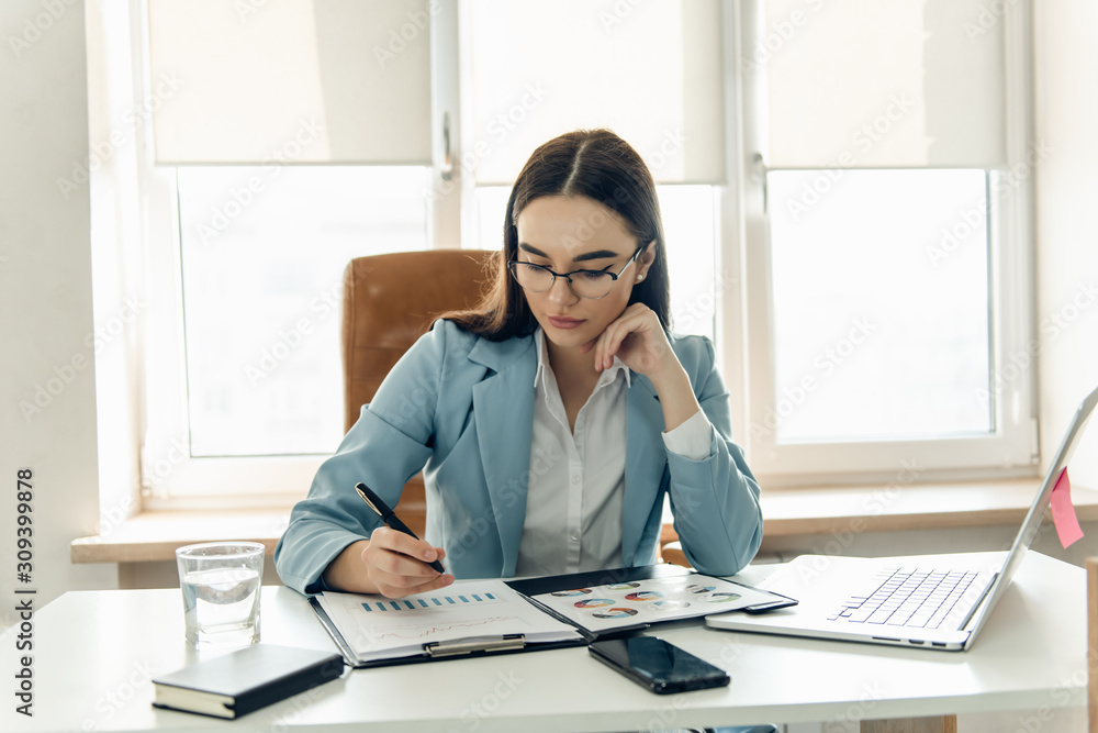 Focused businesswoman working with chart. Focused business woman working looking at laptop making notes. Focused businesswoman working with chart. Focused business woman working looking at laptop making notes.