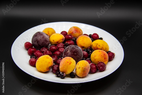 A Berry mix from frozen currant  apricot  plum  cherry on the white plate. Frozen Berries from freezer. A background with frozen plum  currant  apricot and cherry. A healthy Berries on the background