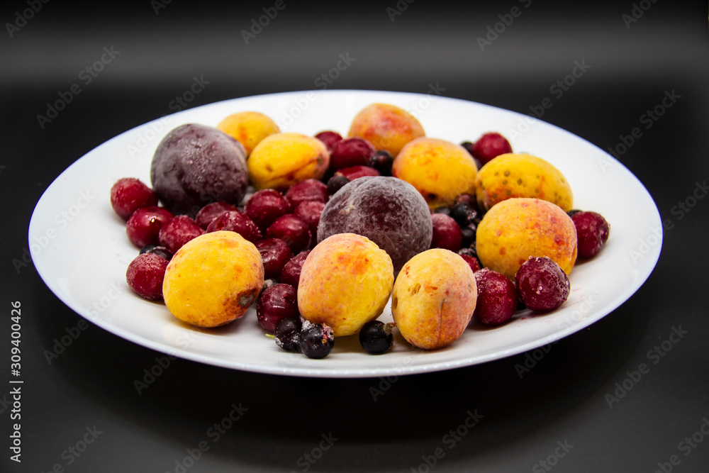 A Berry mix from frozen currant, apricot, plum, cherry on the white plate. Frozen Berries from freezer. A background with frozen plum, currant, apricot and cherry. A healthy Berries on the background