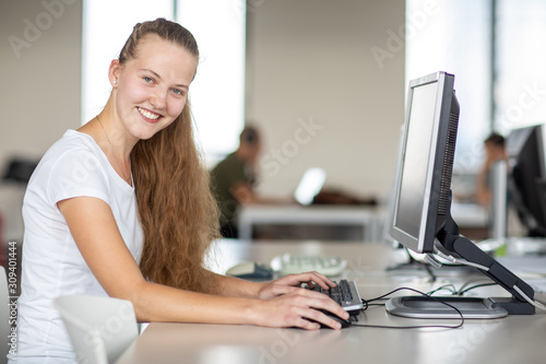 Cute female university highschool student using a desktop computer in a library study room at the university