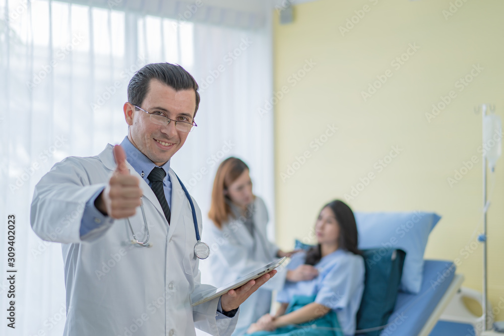 A professional doctor standing in a room with a patient lying in bed with an assistant doctor to prepare for a patient check up.