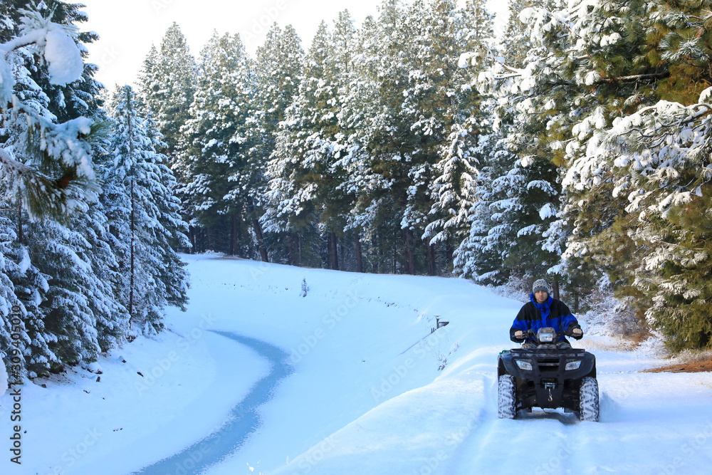 Man riding snowmobile or fourwheeler on the country side trail near water canal.
