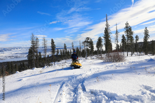 Man riding snomobile in the mountains near cabin houses and trees.