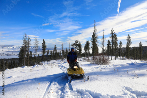 Man riding snomobile in the mountains near cabin houses and trees. photo