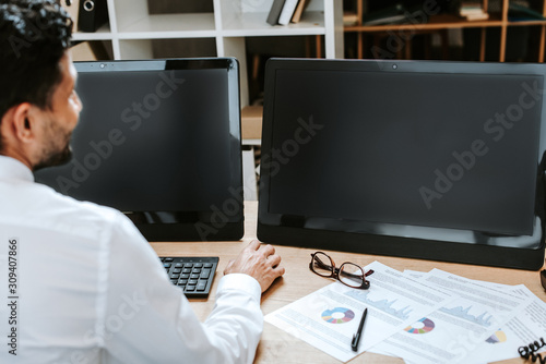 selective focus of bi-racial trader sitting at table with computers