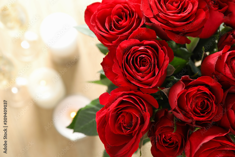 Red roses, close up. Blurred background with candles and glasses of champagne. Space for text Red roses, close up. Blurred background with candles and glasses of champagne. Space for text